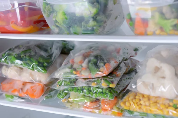 Plastic bags and containers with frozen vegetables in refrigerator 